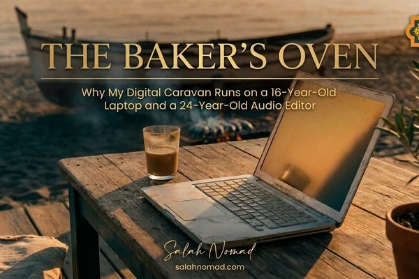 A worn 2010 silver laptop open on a rustic wooden terrace table on a Málaga beach at sunset, a glass of café con leche beside it, a potted olive tree at the frame's edge, and a fishing boat with olive-wood smoke rising from grilling sardines in the soft-focus background.